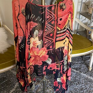 May include: A sheer black and red long-sleeved top with an abstract geometric and floral print. The top has a scoop neck and a loose, flowing fit.