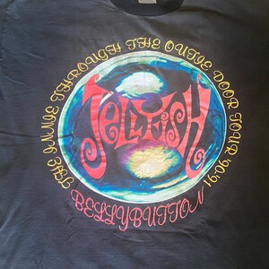 May include: Black t-shirt with a circular graphic of a blue and green orb with the word "Jellyfish" in red and yellow letters. The text "The  Voyage Through The Outer Door Tour 1991-92" and "Belly Button" are in yellow letters around the orb.
