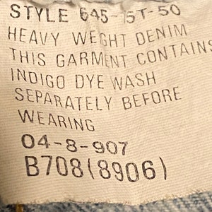 K&ouml;nnte beinhalten: Ein wei&szlig;es Etikett mit schwarzem Text, der "STYLE 645-1ST-50 HEAVY WEIGHT DENIM THIS GARMENT CONTAINS INDIGO DYE WASH SEPARATELY BEFORE WEARING 04-8-907 B708(8906)" lautet.