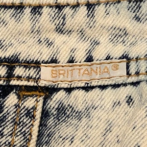 K&ouml;nnte beinhalten: Nahaufnahme eines wei&szlig;en und blauen Jeansstoffes mit einem goldenen Etikett, auf dem "BRITANNIA&reg;" steht.