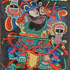 May include: Embroidered denim patch featuring a colorful, mythical figure with a purple beard, holding a sword and standing on a dragon. The figure is wearing a green and red robe with gold accents.