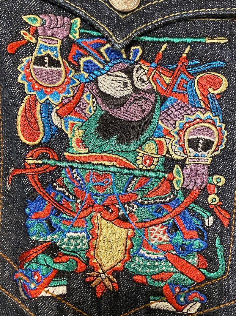 May include: Embroidered denim patch featuring a colorful, mythical figure with a purple beard, holding a sword and standing on a dragon. The figure is wearing a green and red robe with gold accents.