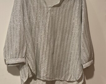 May include: A silver, long-sleeved blouse with vertical stripes and a V-neck. The blouse has a loose fit and three-quarter sleeves. The fabric has a subtle shimmer. The blouse is hanging on a black hanger.