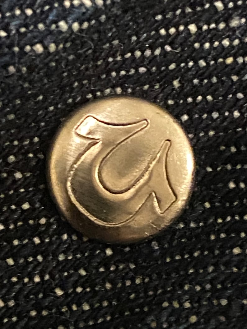 May include: A close-up of a gold-colored metal button with the letter "U" embossed on it.