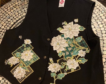 May include: A black sleeveless vest with a green, white, and gold floral design. The vest has a V-neck and buttons down the front.