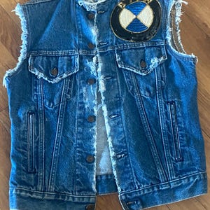Può includere: Un giubbotto di jeans blu con orlo sfrangiato e un grande logo BMW ricamato sul retro.