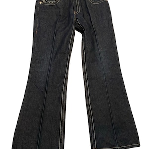 May include: Dark blue denim jeans with a bootcut leg opening. The jeans have a light brown stitching detail and a small leather patch on the back.