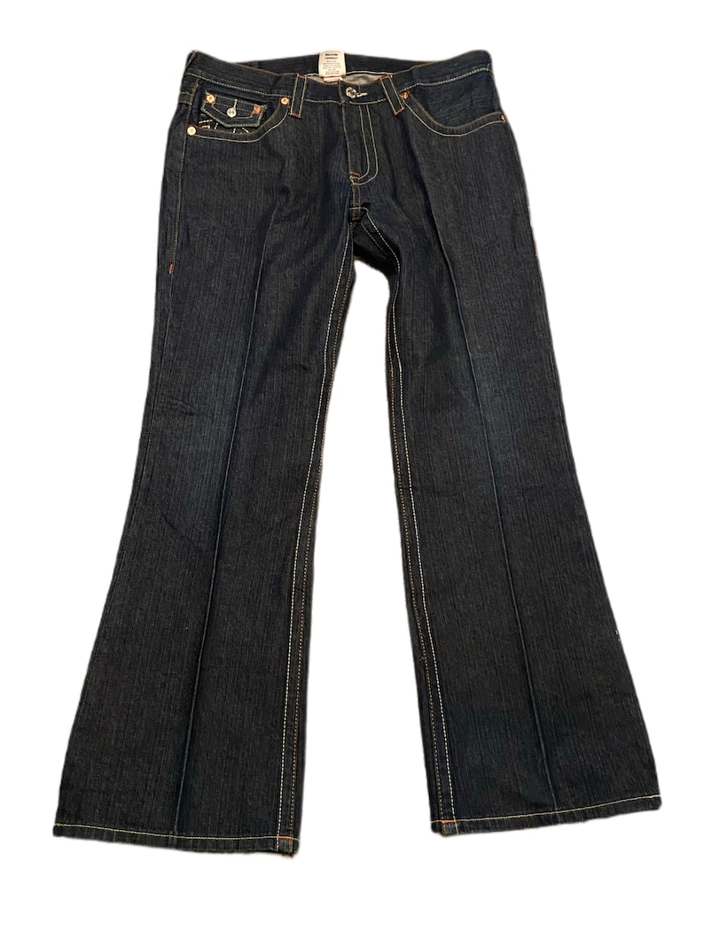 May include: Dark blue denim jeans with a bootcut leg opening. The jeans have a light brown stitching detail and a small leather patch on the back.