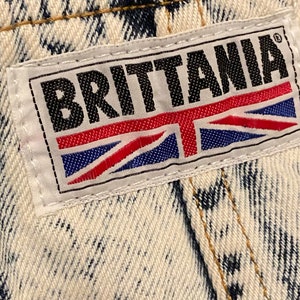 K&ouml;nnte beinhalten: Ein wei&szlig;er Jeans-Patch mit schwarzem Text, der "BRITANNIA" lautet, und einer rot-wei&szlig;-blauen Union Jack-Flagge.