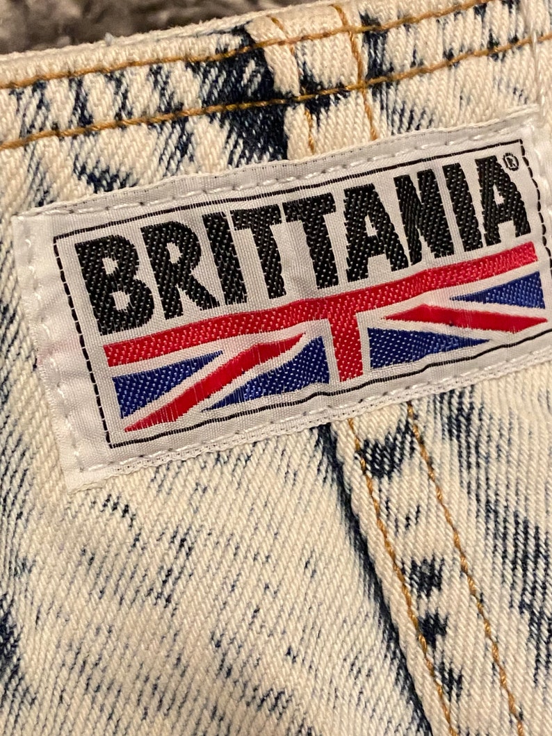 K&ouml;nnte beinhalten: Ein wei&szlig;er Jeans-Patch mit schwarzem Text, der "BRITANNIA" lautet, und einer rot-wei&szlig;-blauen Union Jack-Flagge.