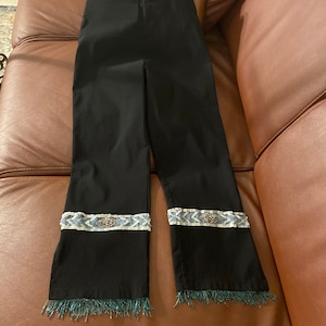 Puede incluir: Pantalones negros con un ribete de cuentas azules y blancas y flecos azules en la parte inferior.