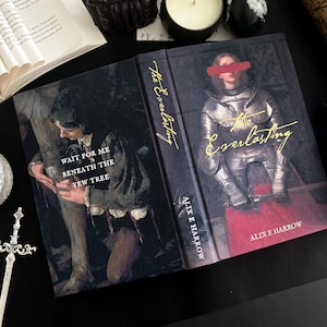 May include: Hardcover book titled "The Everlasting" by Alix E. Harrow. The cover features a woman in armor with a red bar over her eyes. The spine and cover text are gold. The other side of the book has a painting with the text "Wait for me beneath the yew tree."