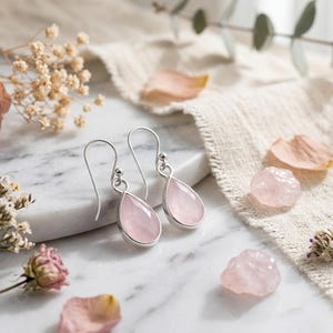 Peut inclure: Une paire de boucles d'oreilles pendantes en argent avec des pierres facettées en forme de goutte d'un rose pâle. Les boucles d'oreilles sont dotées de crochets en argent simples et d'une petite boucle reliant la monture à l'attache.
