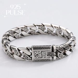 May include: A silver-toned curb chain bracelet featuring intricate scrollwork engravings on each link and a rectangular box clasp. The clasp is detailed with ornate floral-inspired patterns. The text 925 PULSE is visible in the upper left corner.