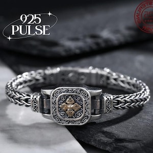 May include: A silver bracelet featuring a woven chain design and a central rectangular clasp with intricate filigree patterns and a gold-toned embossed emblem. The text 925 PULSE is visible in the upper left corner of the image.