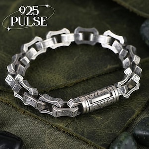 May include: A silver chain bracelet featuring rectangular links with intricate engraved patterns and a cylindrical clasp closure. The text 925 PULSE is visible in the upper left corner. The bracelet is constructed from polished sterling silver metal.