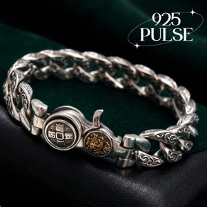May include: A silver curb chain bracelet featuring intricate engraved scrollwork on each link. The clasp mechanism includes a circular silver component with Chinese characters and a smaller, adjacent circular gold-toned accent piece.