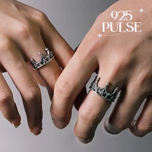 May include: Two silver-toned rings shaped like crowns with intricate detailing and dark oxidised accents. The text 925 PULSE is visible in the upper right corner. The rings feature pointed tips and a band design that mimics a royal crown structure.