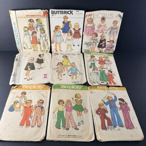 May include: A collection of nine vintage sewing pattern envelopes featuring illustrations of children's clothing. The envelopes include brands such as McCall's, Butterick, and Simplicity, displaying various outfits like dresses, overalls, and pants.