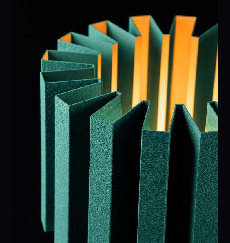 Puede incluir: Una pantalla de l&aacute;mpara cil&iacute;ndrica con un exterior plisado en un color verde bosque profundo con un acabado texturizado. El interior de la pantalla es de un naranja brillante y c&aacute;lido, creando un fuerte contraste al iluminar los pliegues.