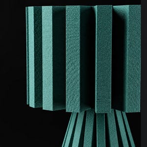 Puede incluir: Una l&aacute;mpara de color verde azulado con una pantalla texturizada y plisada, y una base a juego con paneles rectangulares verticales. La estructura est&aacute; compuesta por m&uacute;ltiples segmentos r&iacute;gidos similares a espuma en un patr&oacute;n geom&eacute;trico.