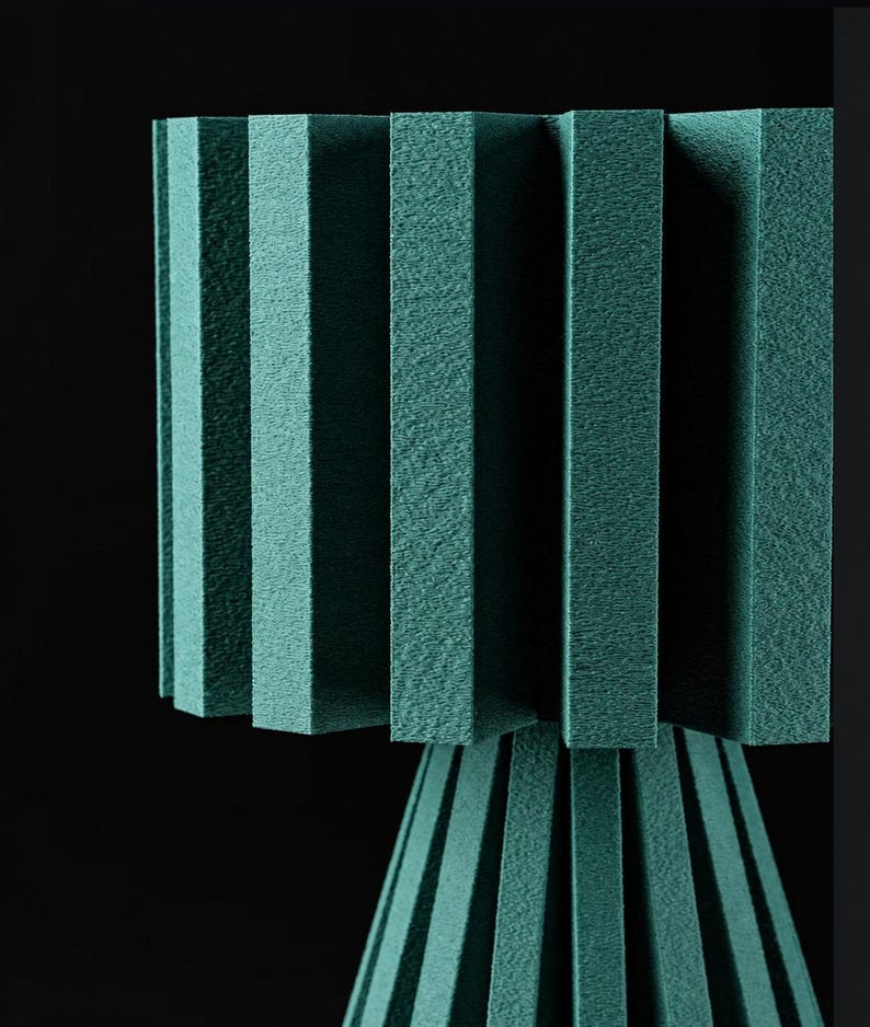 Puede incluir: Una l&aacute;mpara de color verde azulado con una pantalla texturizada y plisada, y una base a juego con paneles rectangulares verticales. La estructura est&aacute; compuesta por m&uacute;ltiples segmentos r&iacute;gidos similares a espuma en un patr&oacute;n geom&eacute;trico.