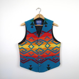 May include: A Pendleton brand vest featuring a vibrant geometric pattern in shades of turquoise, red, orange, and yellow. The sleeveless garment has a V-neckline, a black interior lining, and four silver-toned buttons down the front closure.