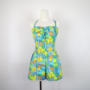 May include: A sleeveless romper featuring a vibrant floral pattern in shades of yellow, orange, and light blue against a medium blue background, with a central tie detail at the bodice, a straight neckline, and thin shoulder straps.