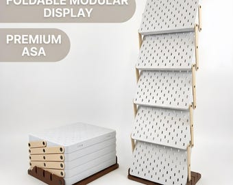 Könnte beinhalten: Ein klappbarer, modularer Präsentationsständer mit fünf weißen, rechteckigen Lochplatten-Regalen, die durch hellbraune Holzseitenteile verbunden sind, daneben eine zusammengeklappte Einheit. Der Text FOLDABLE MODULAR DISPLAY und PREMIUM ASA ist sichtbar.