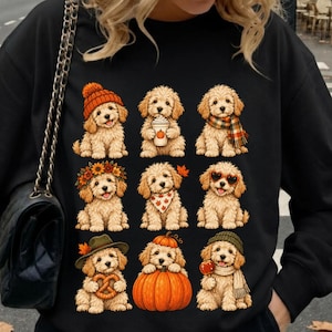 Puede incluir: Una sudadera negra de manga larga con un estampado gráfico de nueve cachorros de color marrón claro en varios atuendos y poses otoñales, incluyendo gorros, bufandas, y sosteniendo calabazas, un pretzel y una taza de café con diseño.