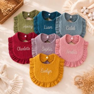 Può includere: Una collezione di sette bavaglini con volant per neonati in verde oliva, blu scuro, blu ardesia, bordeaux, lavanda, rosa antico e giallo senape. Ogni bavaglino presenta una chiusura a pressione bianca ed è ricamato con un nome: Henry, Liam, Caleb, Charlotte, Sophia, Amelia o Evelyn.