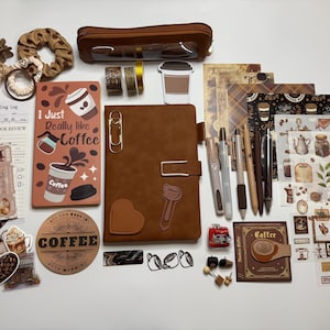 May include: A collection of coffee-themed stationery including a brown notebook, a pencil case, various stickers, washi tape, pens, and hair accessories. The notebook cover features the text I Just Really like Coffee with illustrations of coffee cups.