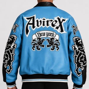 Puede incluir: Una chaqueta azul claro con mangas de cuero negro y cuello negro. La parte posterior presenta un gran bordado en blanco y negro con el texto Avirex y New York, junto a dos gráficos de leones negros. Puños y dobladillo acanalados con rayas blancas.