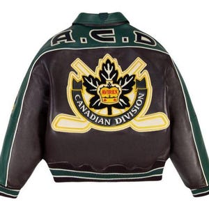 May include: A dark brown and green leather varsity jacket featuring a large embroidered patch on the back with a maple leaf, crossed hockey sticks, and the text "AVIREX CANADIAN DIVISION". The collar is green, and the text "A.C.D" is embroidered.