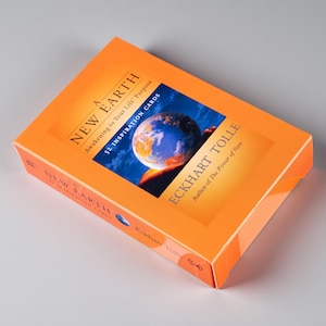 May include: A rectangular box of A New Earth 52 Inspiration Cards by Eckhart Tolle. The bright orange packaging features a central image of the Earth from space, with the title and author name printed in black text on the front and side panels.