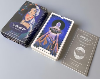 May include: A Wake Me Up Tarot deck set featuring a rectangular box with a character illustration, a deck of cards with a Death card showing a figure with a moth, and a gray guidebook with a moth graphic and the text Wake Me Up Tarot Guidebook.