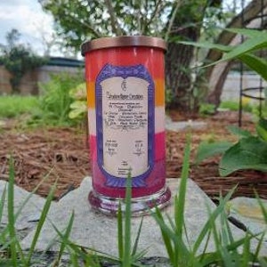 Op de afbeelding: Een meerkleurige kaars in een glazen pot met een koperen deksel. De kaars is gelaagd met rode, oranje, gele en paarse was. Het etiket op de pot vermeldt "Southern Charm Creations" en geeft de geur van de kaars aan als "Oranje, Kaneel en Vanille".
