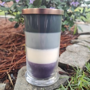 May include: A layered candle in a clear glass jar with a copper lid. The candle has four layers of wax: dark gray, light gray, white, and purple.