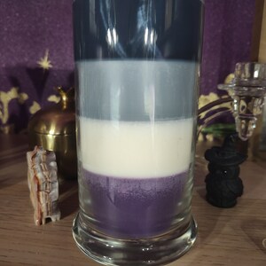 May include: A layered candle in a clear glass jar with a dark blue, light gray, white, and purple wax layers.