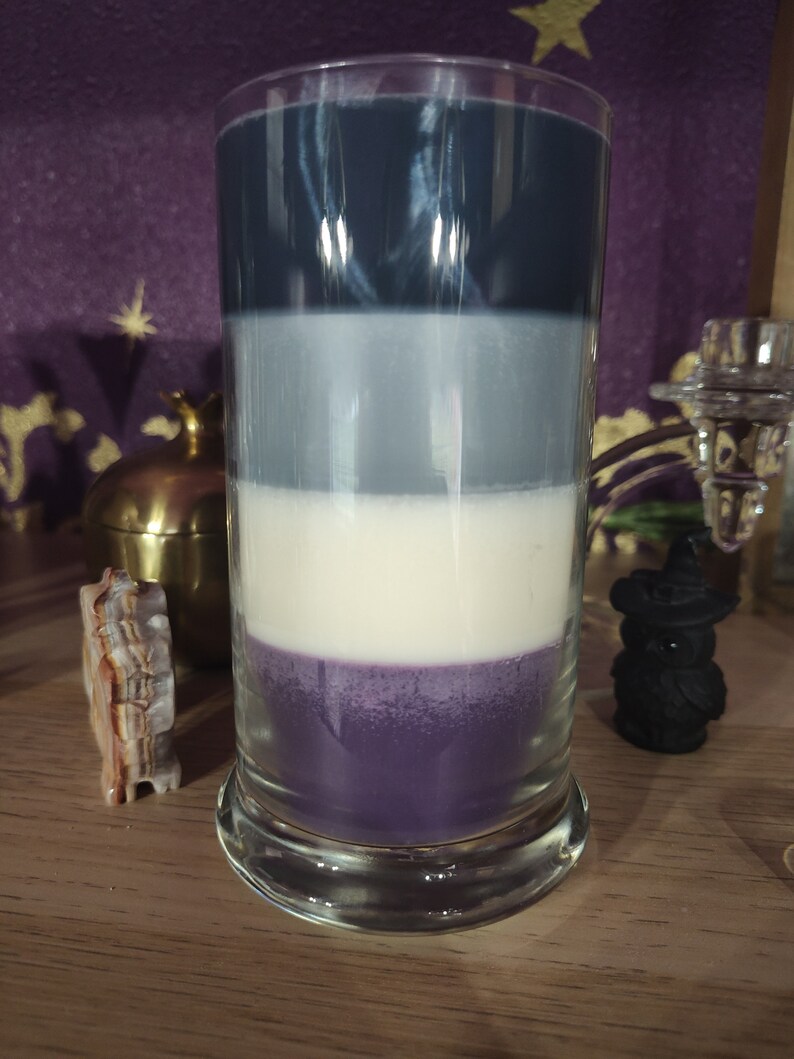 May include: A layered candle in a clear glass jar with a dark blue, light gray, white, and purple wax layers.