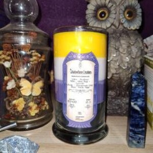 May include: A three-layered candle with yellow, white, and purple wax. The candle has a label that reads "Spellbound Scents" and lists the scent as "Lavender, Eucalyptus, White Tea, Peppermint, and Musk".