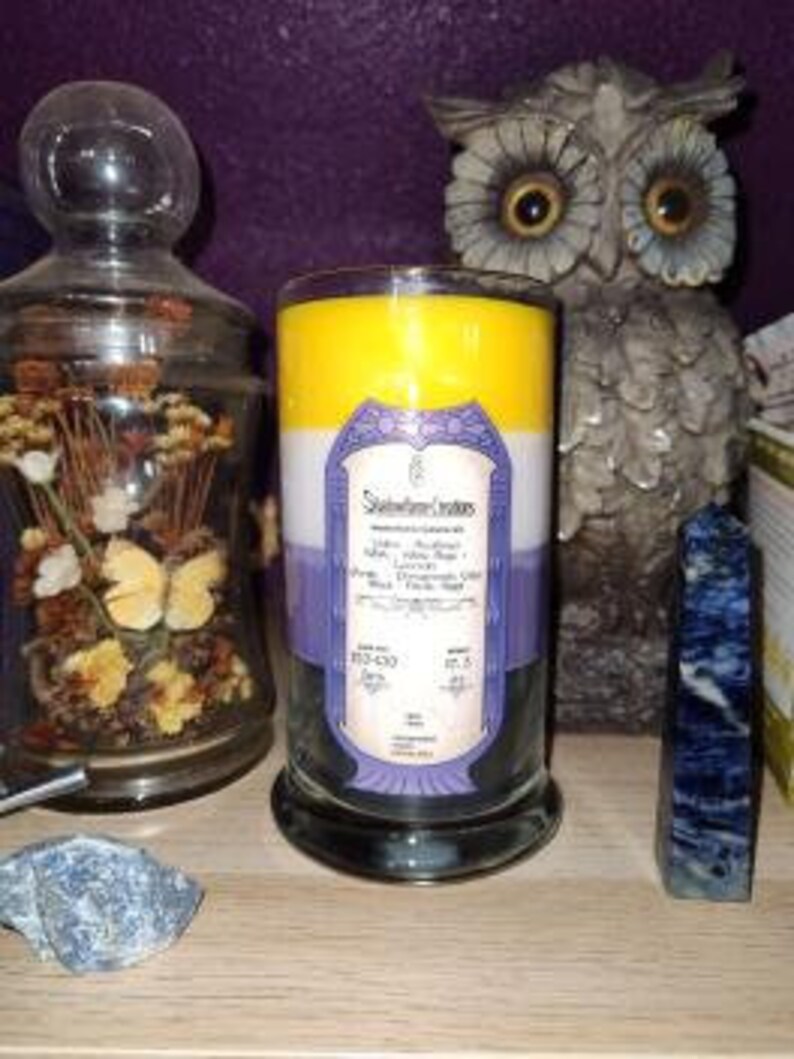May include: A three-layered candle with yellow, white, and purple wax. The candle has a label that reads "Spellbound Scents" and lists the scent as "Lavender, Eucalyptus, White Tea, Peppermint, and Musk".