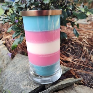 May include: A layered candle with a blue, pink, and white design. The candle is in a clear glass jar with a gold lid.