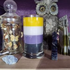 May include: A candle with yellow, white, purple, and black stripes, representing the non-binary pride flag.
