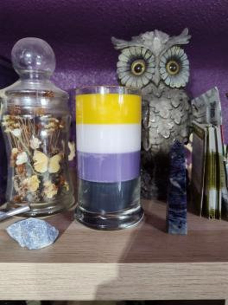 May include: A candle with yellow, white, purple, and black stripes, representing the non-binary pride flag.