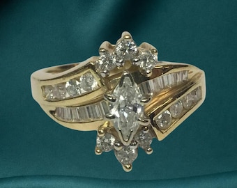 May include: A gold ring featuring a central marquise-cut diamond surrounded by smaller round-cut diamonds. The band includes channel-set baguette diamonds and round-cut diamonds along the sides, creating a multi-stone cluster design.