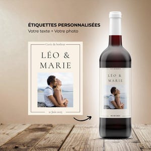 Könnte beinhalten: Eine Weinflasche mit einem personalisierten Etikett mit dem Text "Cuvée du bonheur", "LÉO & MARIE" und "06/09/2021" über einem Foto eines Paares, das sich am Wasser umarmt. Das Etikettendesign wird separat mit dem Datum "21 Juin 2025" gezeigt.