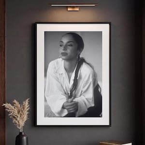 May include: A black and white framed portrait of a person with long dark hair wearing a white collared shirt and hoop earrings. The person is captured in a medium shot, looking away from the camera with hands clasped together in front.