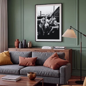 Pu&ograve; includere: Una fotografia in bianco e nero incorniciata che ritrae quattro persone che ridono insieme su un tetto, esposta su una parete verde salvia sopra una credenza in legno. La scena cattura un momento spontaneo con lo skyline urbano sullo sfondo.