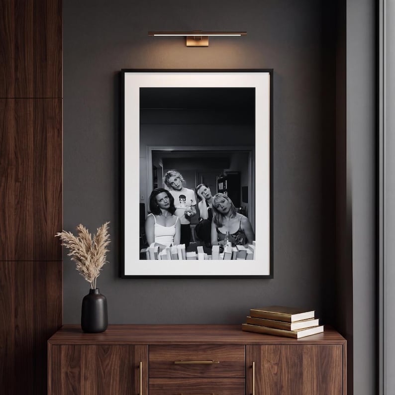 Op de afbeelding: Een zwart-wit ingelijste wandkunstprint met een groep van vier personen in een kamer. De print wordt weergegeven in een dunne zwarte lijst met een brede witte passe-partout. De afbeelding toont de onderwerpen in een informele setting met diverse items.